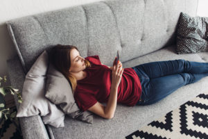 Woman lying on the sofa and using smartphone at home.