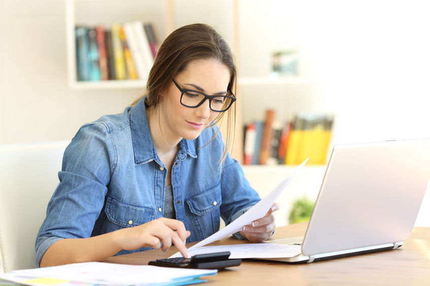 Wommen in glasses using calculator and laptop to calculate her apartment budget