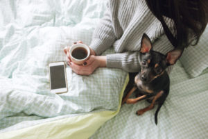 Woman snuggled up with a small dog, a cup of coffee and a smart phone.